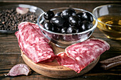 A tasty Mediterranean antipasto with Spanish salami, black olives, garlic and olive oil. Perfect starter arrangement on a rustic wooden table.