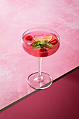A refreshing pink gin cocktail, garnished with fresh mint, a slice of lemon and juicy raspberries, served in an elegant glass against a bright pink backdrop