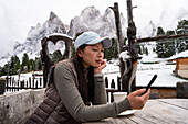 An Asian woman enjoys quiet moments on a wooden bench on the Geisleralm, Italy Snow-capped Dolomites and a rustic heart-shaped carving emphasise the picturesque Alpine backdrop