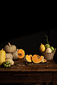 Various pumpkins and chayote with bright orange and green tones, arranged on a rustic wooden table against a dark background reminiscent of an autumnal harvest scene.