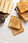 Golden toast from above next to a bowl of blueberries and raspberries on a rustic wooden board with a fabric background.
