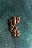 Top view of homemade milk chocolate bars combined with a rich pistachio paste, also known as Dubai chocolate, arranged on a textured green background.
