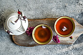 White teapot with two teacups, decorated with pink chrysanthemum flowers on a rustic wooden board Elegant tea service with floral accents on a textured grey surface
