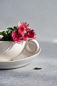 A delicate arrangement of bright pink flowers in a white teacup against a soft, textured background - perfect for decorations or floral designs