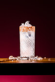 A Paloma cocktail in a patterned glass decorated with a salt rim and filled with refreshing ice. The drink is set against an atmospheric, dark background that emphasises its vibrant presentation