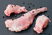 Close-up of fresh, raw pieces of rabbit meat on a dark stone, sprinkled with whole black peppercorns Ideal for culinary or gourmet presentations and food-related content