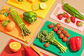 A colourful selection of fresh fruit and vegetables on multi-coloured chopping boards. These include strawberries, oranges, tomatoes, asparagus, broccoli, peppers and limes.
