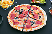 A freshly baked chorizo pizza topped with black olives, presented on a black board Cut into pieces, perfect for sharing or enjoying individually