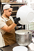 An eager baker in an apron and cap prepares the dough in a busy Italian bakery kitchen. The backdrop includes professional baking tools and creates an authentic culinary atmosphere