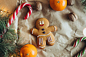 A cheerful gingerbread man decorated with icing, surrounded by candy canes, walnuts, oranges and fir branches creates a cosy, festive atmosphere
