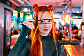 A young woman with lively hair and a stylish outfit enjoys her time at an Asian food market, playfully holding chopsticks in her hand The colourful, lively market atmosphere surrounds her