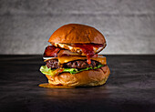 A delicious burger with crispy bacon, fried egg and melted cheese, served on a fresh bed of lettuce with a juicy beef patty, perfect for gourmet food lovers.