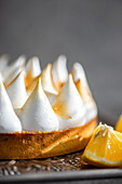 Close-up of a homemade lemon tart, showing the golden brown tips of the toasted meringue. The dessert rests on a decorative plate with fresh lemon slices nearby.