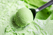 Close-up of a perfectly moulded, homemade pistachio ice cream spoon in a metal spoon. The creamy texture and bright colour make it an inviting treat for dessert lovers.