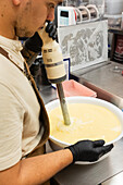 A skilful baker uses a hand blender to prepare dough in a large bowl The setting is a busy Italian bakery where the process of baking delicious pastries is shown