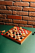 A chessboard on a green surface with chicken nuggets as game pieces. In front of a rustic brick wall, the scene combines food and classic board game aesthetics.
