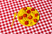 A bright yellow plate with colourful flowers stands on a classic red and white checked tablecloth. A yellow fork completes the lively picnic scene.