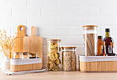 Stylish kitchen interior with wooden chopping boards, jars of dried food and bottles of oil against a white brick wall.