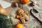 An adorable gingerbread man surrounded by festive elements such as a candy cane, nuts, mandarins, fir branches and twinkling lights that evoke the Christmas spirit
