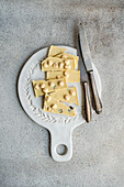 View from above of a white chocolate bar cut into pieces and placed with an old knife on an ornate vintage chopping board, showing a rustic, textured concrete background.
