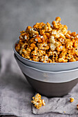 Grey bowl filled with crunchy, sweet caramel popcorn, placed on a soft, grey cloth.