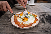 Close-up of a delicious, rustic meal in the restaurant of the Geisleralm in the Dolomites, Italy A plate of eggs and prosciutto with chives on a wooden table