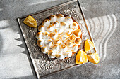 View from above of a homemade lemon cake on a decorative tray, surrounded by lemon wedges. The dessert is beautifully lit by natural sunlight and casts intricate shadows.