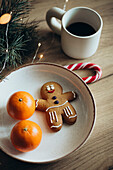A cheerful gingerbread man on a plate with two oranges, accompanied by a candy cane, coffee and festive lights - perfect for celebrating the holidays