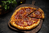 A delicious homemade pepperoni pizza lies on a rustic wooden board, surrounded by fresh basil leaves. Baked to perfection, it exudes an inviting aroma and promises a savoury treat.