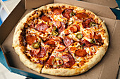 View of a hot, freshly baked pepperoni pizza with jalapenos, served in a simple cardboard box. The crust looks crispy and the cheese seems to have melted perfectly.