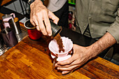 A barista pours freshly ground coffee into a paper filter inserted into a coffee machine. The scene is set on a wooden counter and shows the brewing process of a speciality coffee.