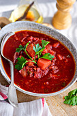 Traditional Ukrainian beetroot soup Borscht, served in a bowl on a rustic table on a sunny day, garnished with fresh parsley.