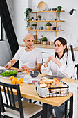 A blind couple sit at a wooden table in a modern kitchen and enjoy a breakfast buffet. They share a moment of bonding and conversation, surrounded by fresh ingredients.