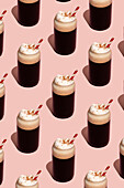 A seamless pattern of frothy coffee cups with cream and a red striped straw on a pale pink background A vibrant, modern design for breakfast themes