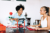 A man and a woman share a romantic dinner at home, with wine, red candles and a rose. The intimate setting emphasises their bond and cheerful mood.