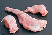 Close-up of fresh, raw rabbit meat pieces on a dark stone surface that highlights the texture and colour, ideal for culinary or butchery themes