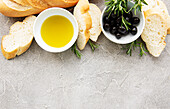 Sliced, fresh, crusty baguette with salt, olive oil, olives and basil on a grey concrete background