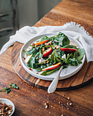 A vibrant and nutritious spinach salad with crunchy apple slices, sprinkled pecans and crumbled cheese, served on a rustic wooden board.