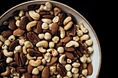 A ceramic bowl with an appetising selection of nuts, including almonds, cashews and hazelnuts, against a dark background that highlights the natural textures