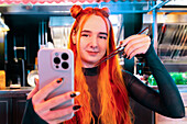 A woman with vibrant hair takes a selfie at an Asian food market, capturing her experience with chopsticks in hand The lively environment emphasises cultural exploration and indulgence