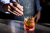 A bartender expertly stirs a whiskey old-fashioned cocktail The clear glass presents a large ice cube that reflects the rich amber colour of the drink Perfect atmosphere for cocktail bars and mixology