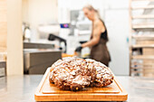 A close-up of freshly baked Italian biscuits on a wooden board in a busy bakery, with a blurred background of a person working, capturing the essence of authentic Italian baking