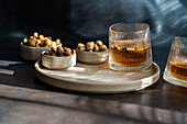 An elegantly prepared spiced cognac cocktail with cinnamon and star anise, paired with various nuts such as almonds, peanuts and hazelnuts, captured in an atmospherically lit setting.