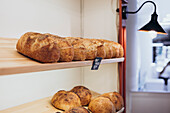 Rustic, freshly baked loaves of bread lie on wooden shelves in a cosy bakery. The golden crusts and warm lighting create an inviting atmosphere