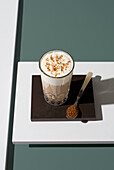 A glass of coffee with soft cream and brown sugar on a dark surface A spoon with brown sugar complements the minimalist decor