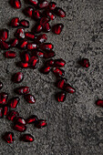 Close-up of glistening red pomegranate seeds scattered across a textured grey stone background, creating a striking contrast of colour and texture that highlights the vibrant beauty of nature.