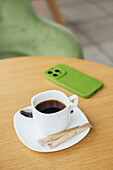 A cosy scene with a cup of black coffee on a wooden table, accompanied by a green smartphone - perfect for illustrating a relaxed coffee break or technology-related content