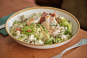 A fresh chicken salad with avocado slices, cheese crumbles, crispy bacon and a boiled egg, served in a bowl, is a healthy snack option on a wooden table
