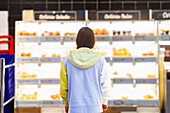 Rear view of an unrecognisable woman standing in front of the bakery section in a supermarket and considering which product to choose.