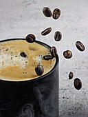 Eine kreative Komposition mit einer dampfenden Tasse heißen Kaffees und in der Luft schwebenden Kaffeebohnen, die ein Gefühl von Wärme und Aroma in einer minimalistischen Umgebung hervorrufen